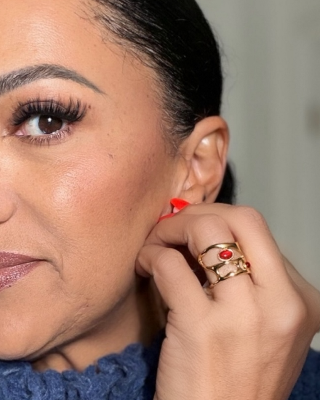 Close-up of a person wearing a gold  ring with a red stone.