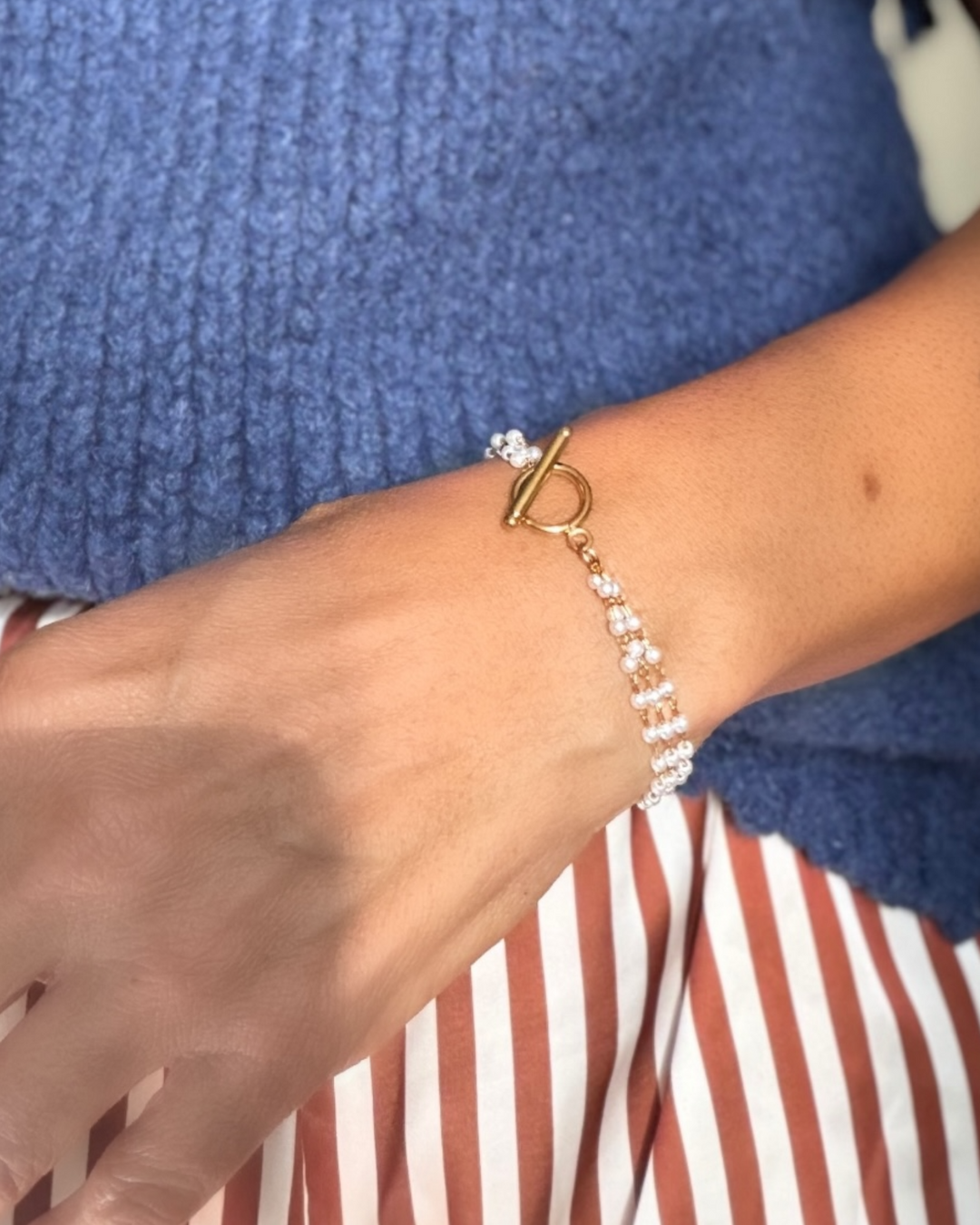 Pearl Bracelet with a gold clasp on a wrist against a blue and red striped background