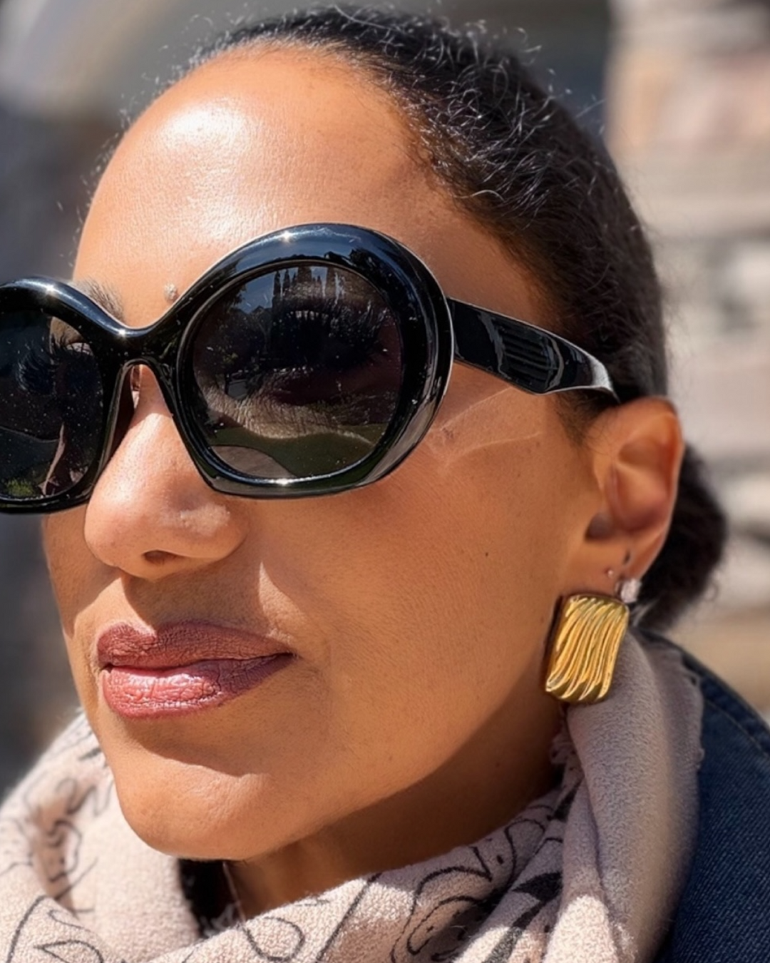 Woman wearing black sunglasses and gold earrings with a blurred background