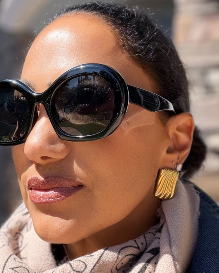 Woman wearing black sunglasses and gold earrings with a blurred background