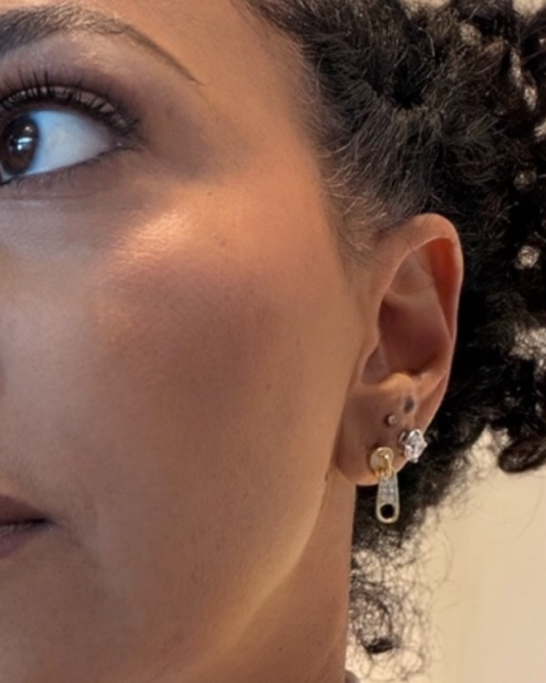 Close-up of a person wearing a gold zipper earring with a clear gemstone.