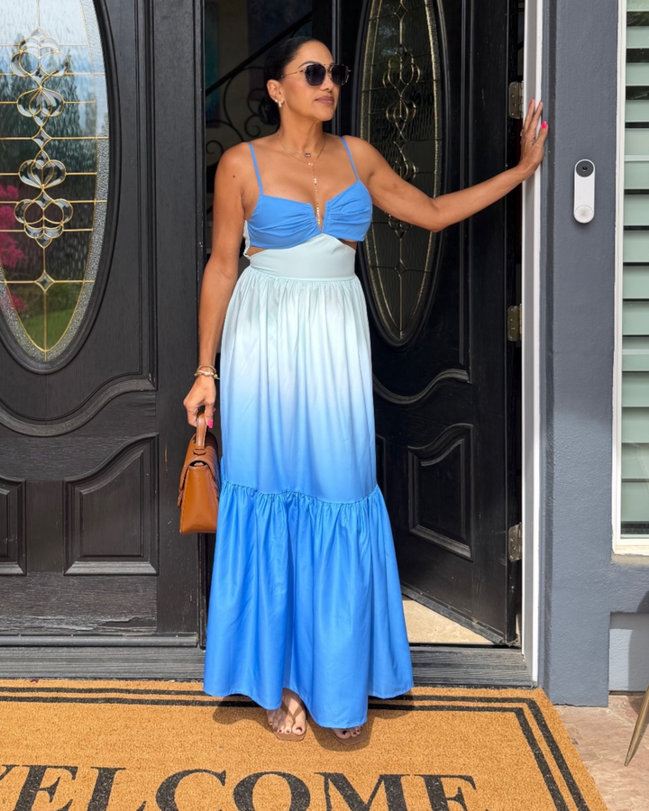 Woman in a blue gradient dress standing in front of a door.
