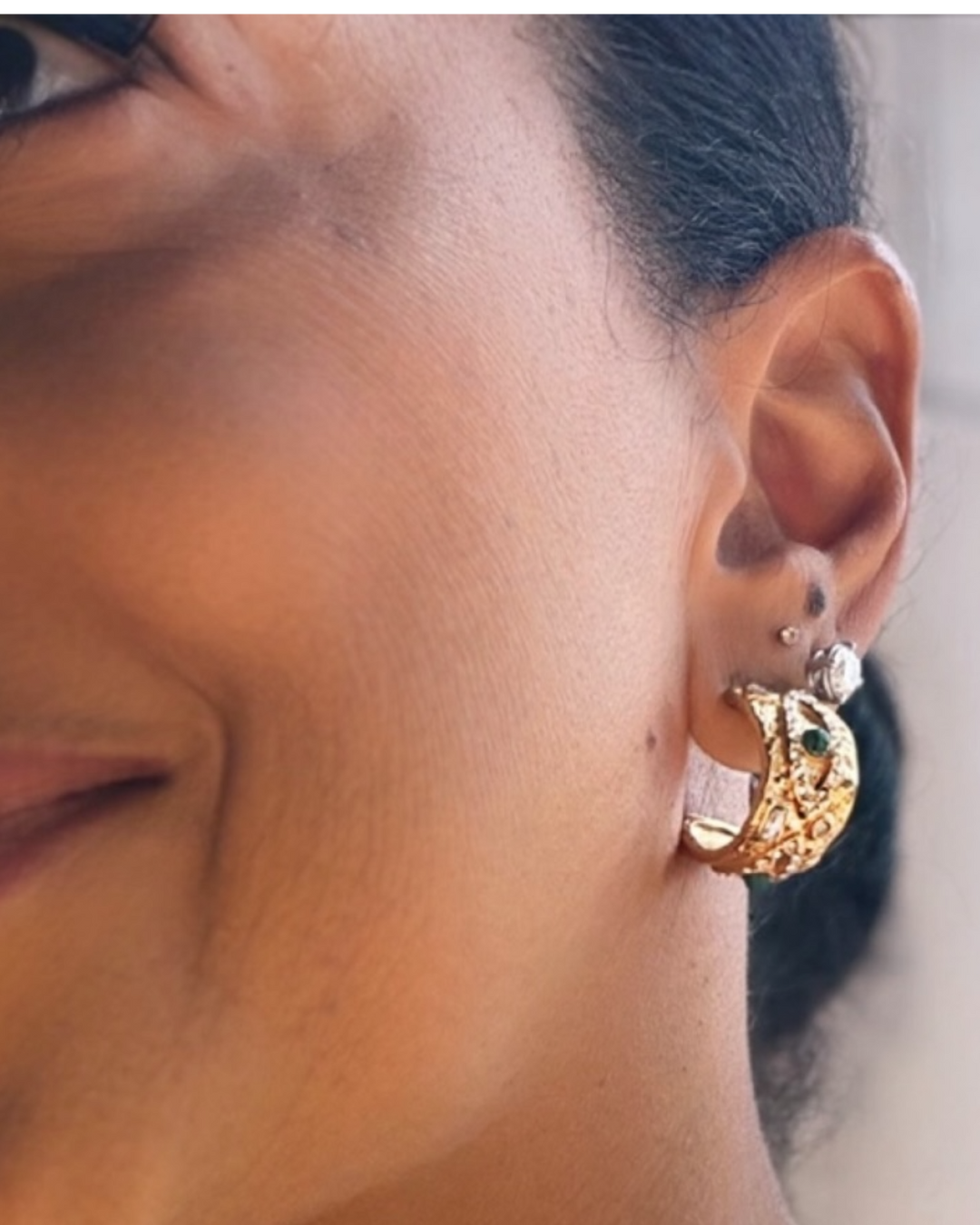 Close-up of an ear wearing a gold earring with a blurred background