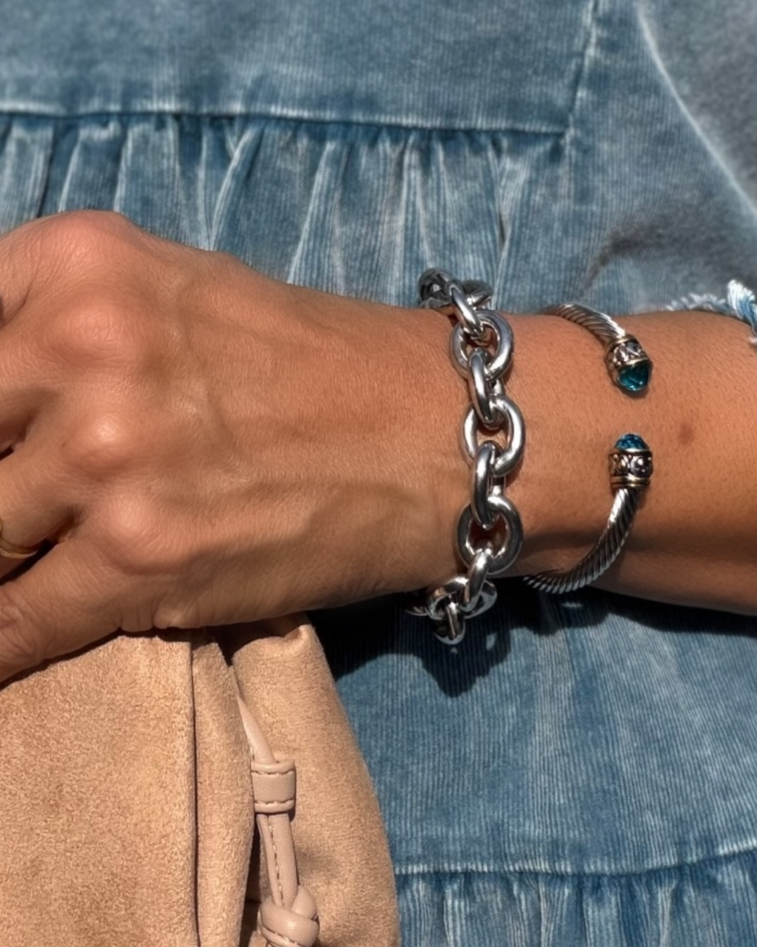 Close-up of a wrist wearing a silver chain bracelet with blue heart charms against a denim background.