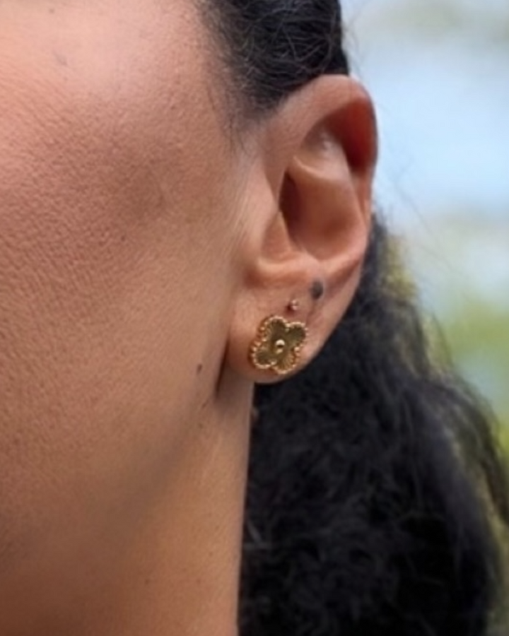 Close-up of an ear wearing a gold flower-shaped earring with a blurred background