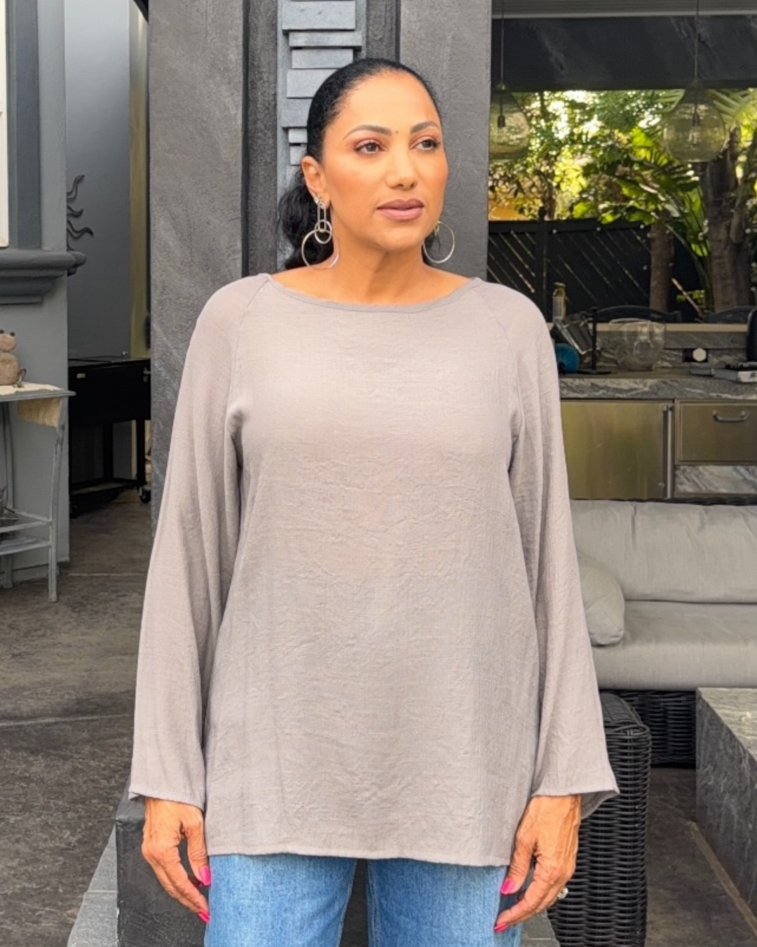 Woman wearing a gray long-sleeve top and blue jeans standing outdoors.