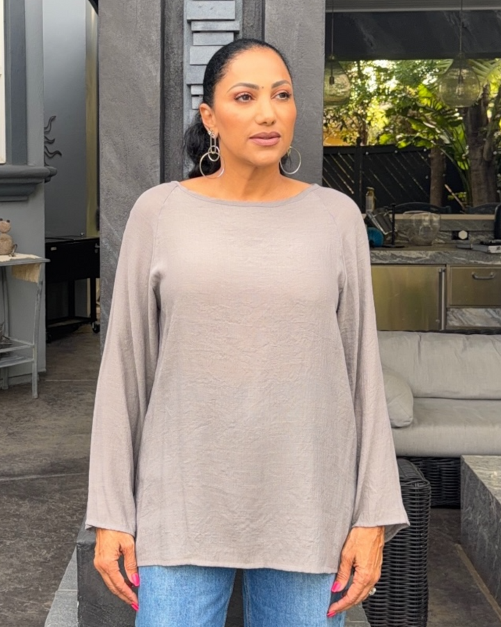 Woman wearing a gray long-sleeve top and blue jeans standing outdoors.