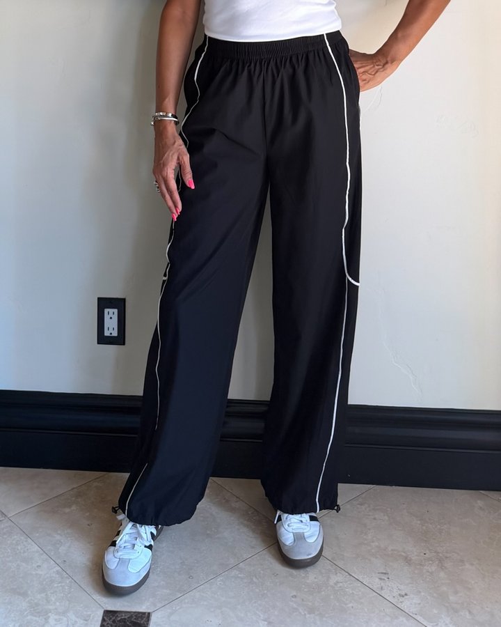 Person wearing black pants with white stripes standing against a wall.