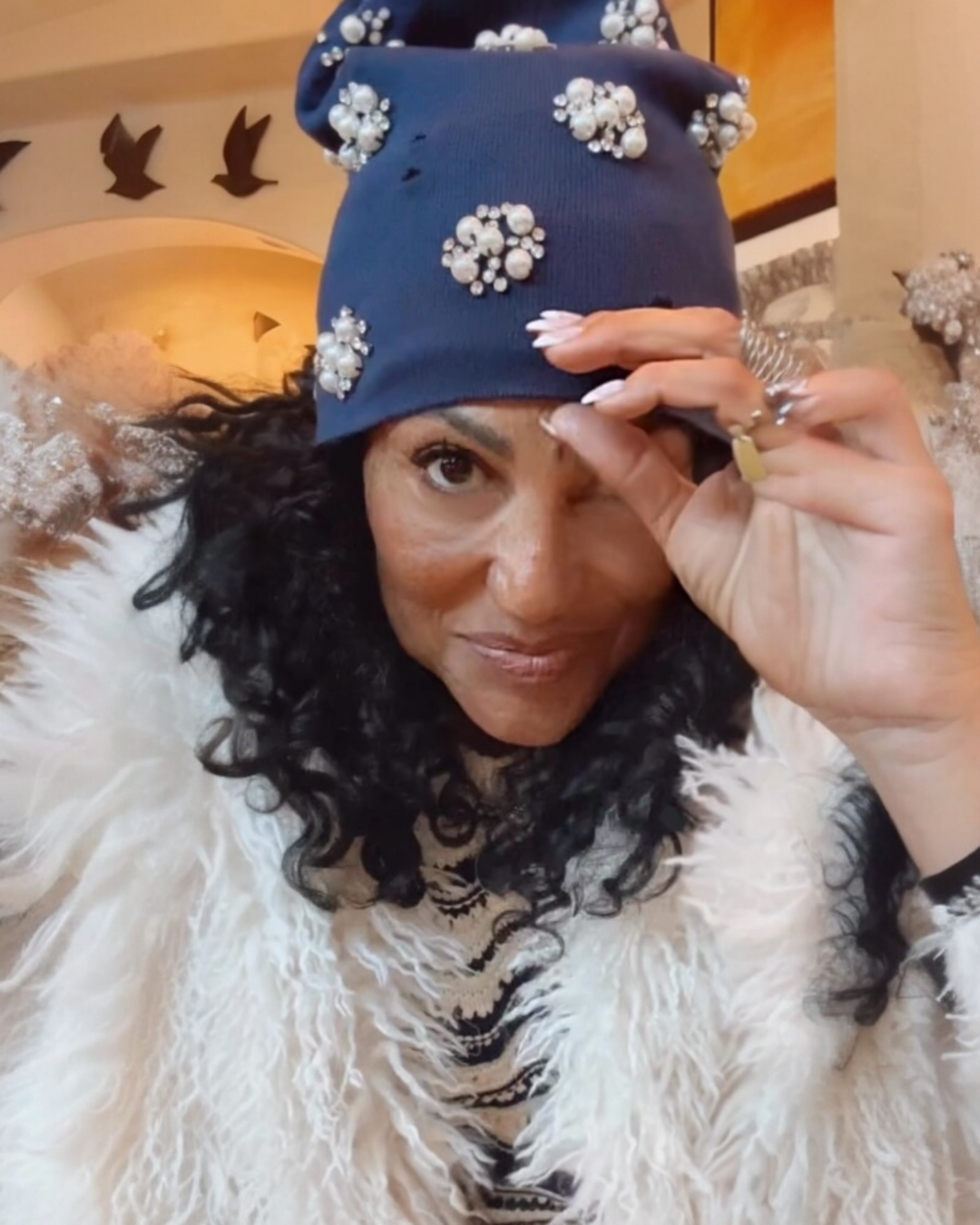 Navy blue knit beanie with pearl and rhinestone embellishments styled for a chic winter look, adding a glam touch to a cozy outfit