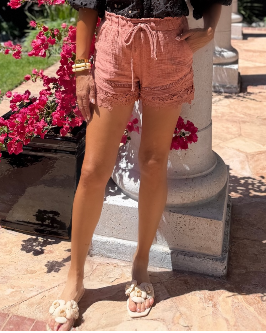 Woman modeling dusty rose textured shorts with lace trim hem and drawstring waist, styled with a floral strapless top and neutral sandals for a chic summer outfit.