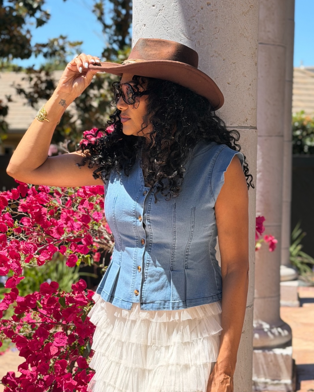 Woman wearing denim peplum vest top with cowboy hat and tiered skirt, side view