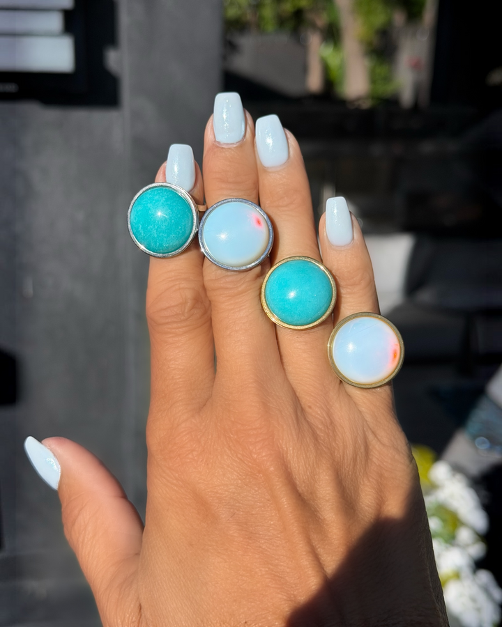 Hand wearing four statement rings featuring Amazonite and white opal stones in gold and silver settings