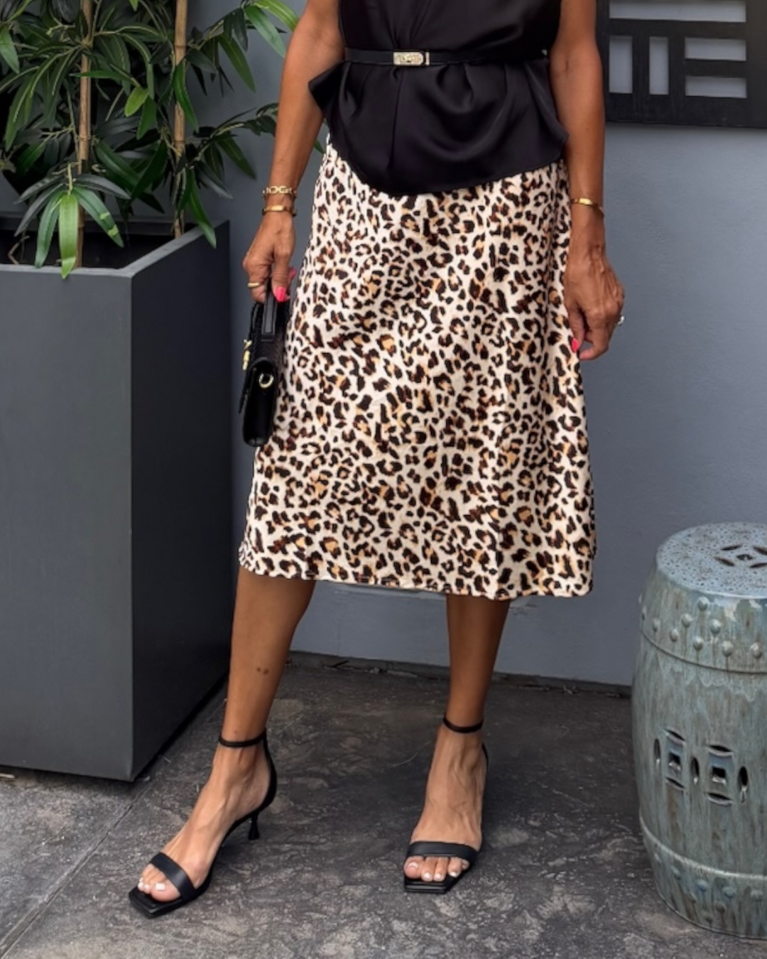 Leopard print midi skirt with high-rise A-line fit, styled with black belted top and black heeled sandals