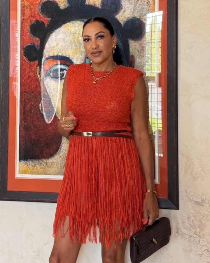Rust orange fringe mini dress with belted waist, styled with gold jewelry and dark clutch