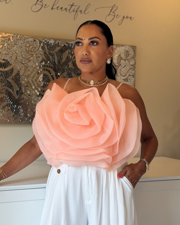 Woman wearing blush pink Bloom Top with oversized rose detail and white trousers