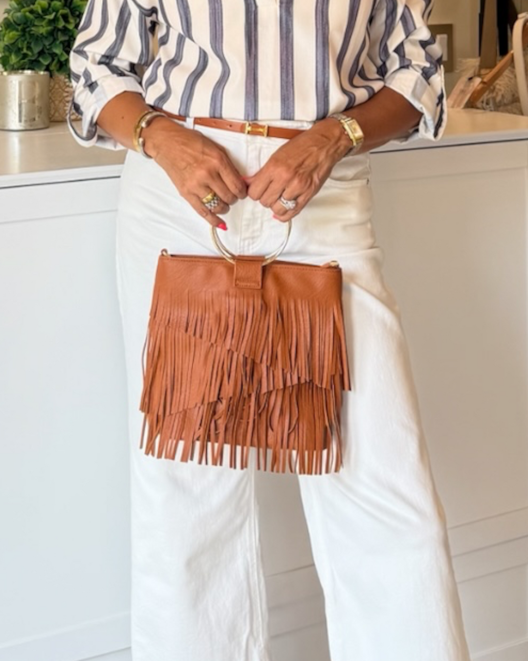 Cognac fringe Austin Fringe Bag with gold ring handle held over white denim