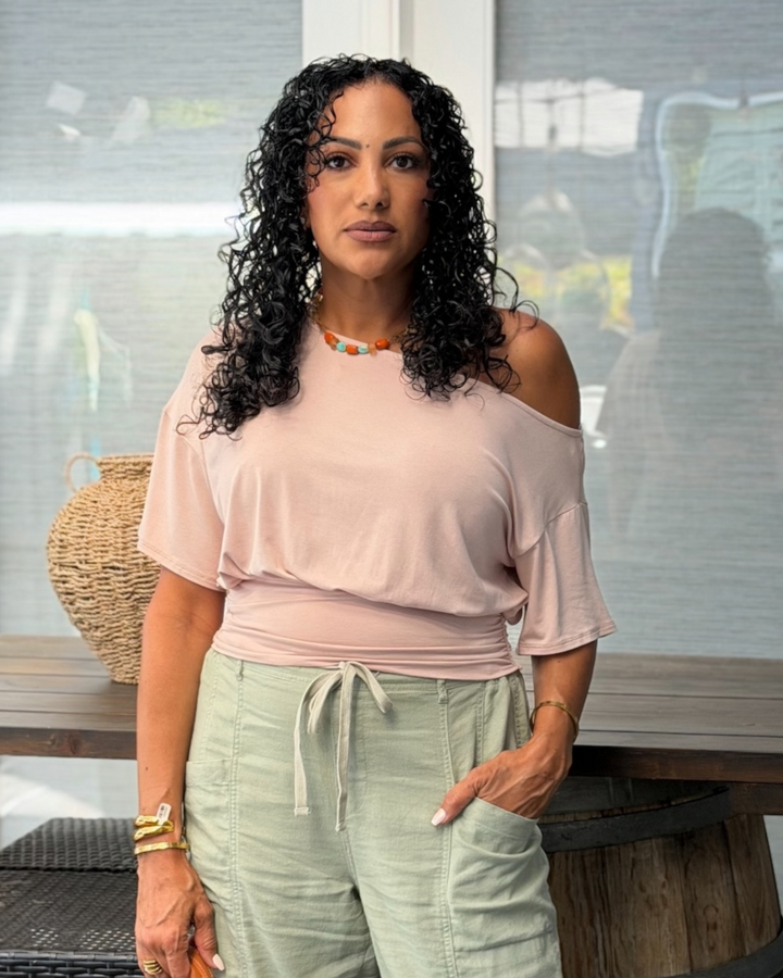 Woman wearing the Blakely blush one-shoulder top with ruched waistband and sage green cargo pants