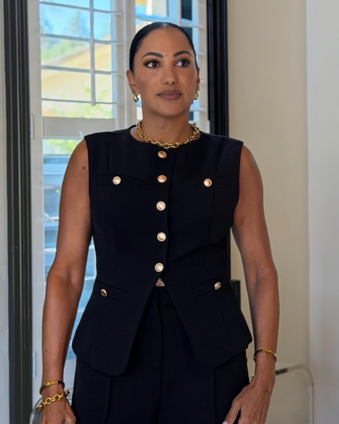 model wearing black button-front vest with gold buttons, close-up detail