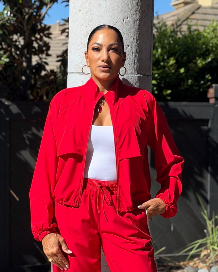 Woman wearing red zip-up windbreaker jacket and matching red wide-leg pants over a white tank top, standing outdoors