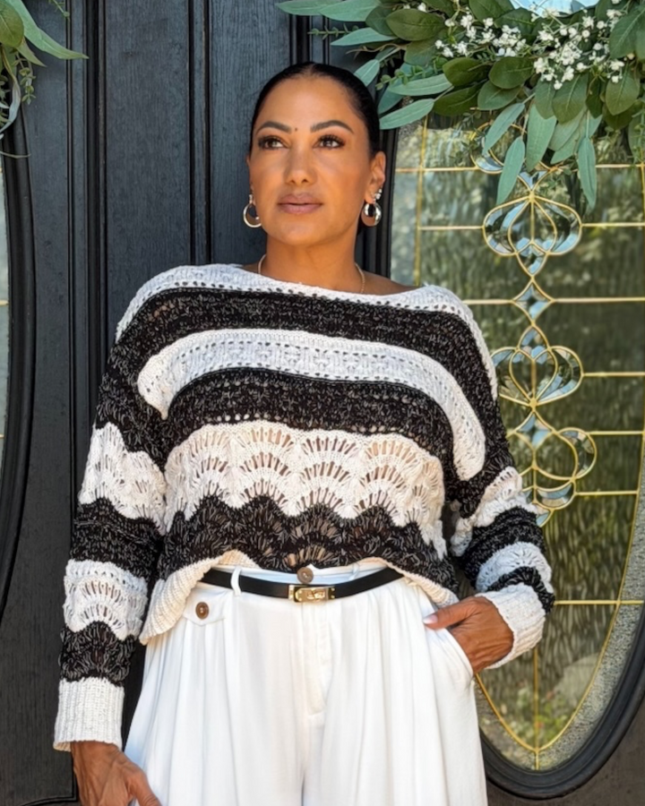 Close-up front view of model wearing black and cream striped open-stitch crochet sweater over white wide-leg pants