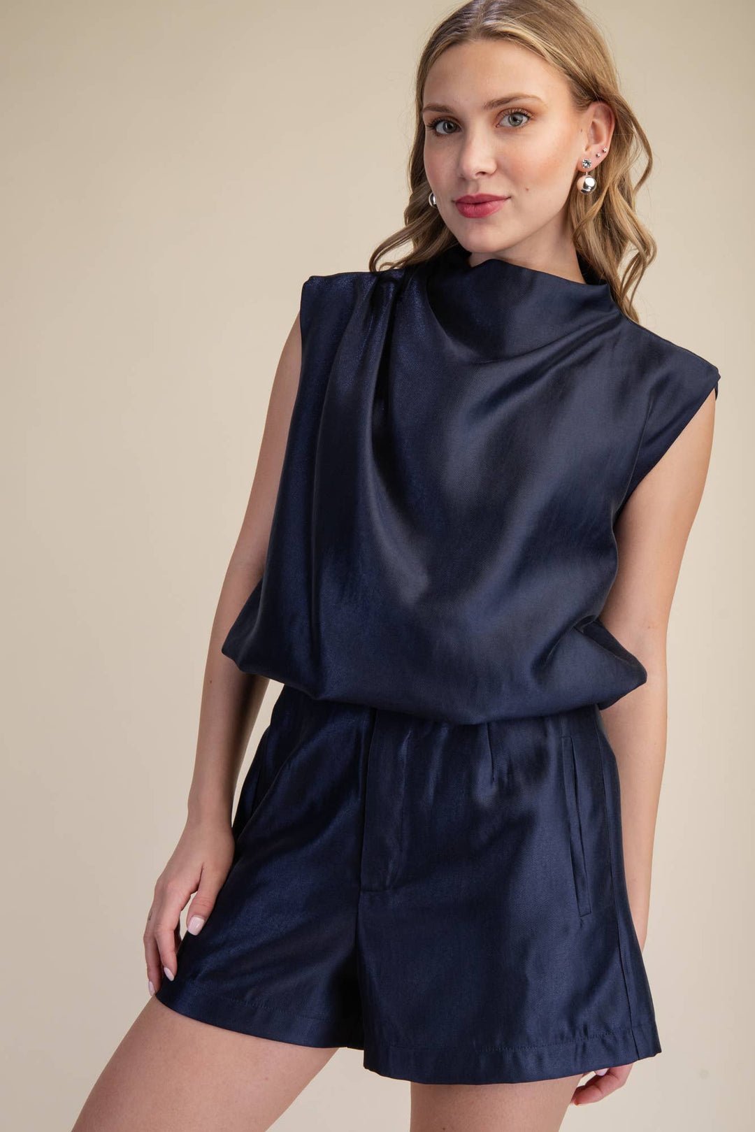 Woman wearing a navy satin sleeveless mock neck bubble top with shoulder gathering and structured cap shoulders, styled with matching navy satin shorts.
