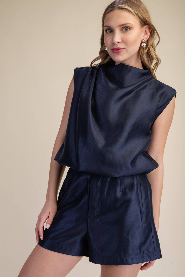 Woman wearing a navy satin sleeveless mock neck bubble top with shoulder gathering and structured cap shoulders, styled with matching navy satin shorts.